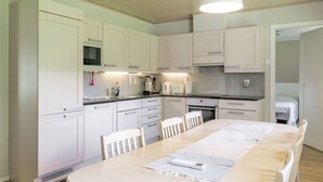 Une cuisine moderne avec des meubles blancs, une table à manger avec des chaises et un luminaire suspendu.