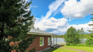 Une maison avec une véranda, une pelouse et un plan d’eau en arrière-plan.