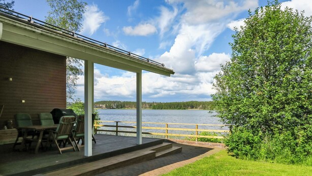 Une terrasse extérieure couverte avec vue sur un lac, un chemin en briques et une pelouse.