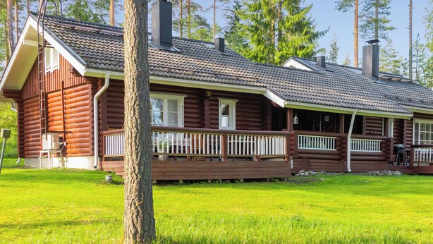 Eine Blockhütte mit Veranda, Schornstein und einem Rasen.
