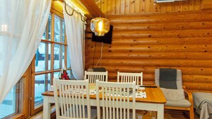 Ein Holzblock-Interieur mit Esstisch, weißen Stühlen, Fernseher und einem Fenster mit Vorhängen.
