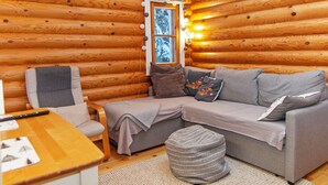 Ein Holzblockhaus-Innenraum mit grauem Sofa, einem Holztisch und einem kleinen Hocker.