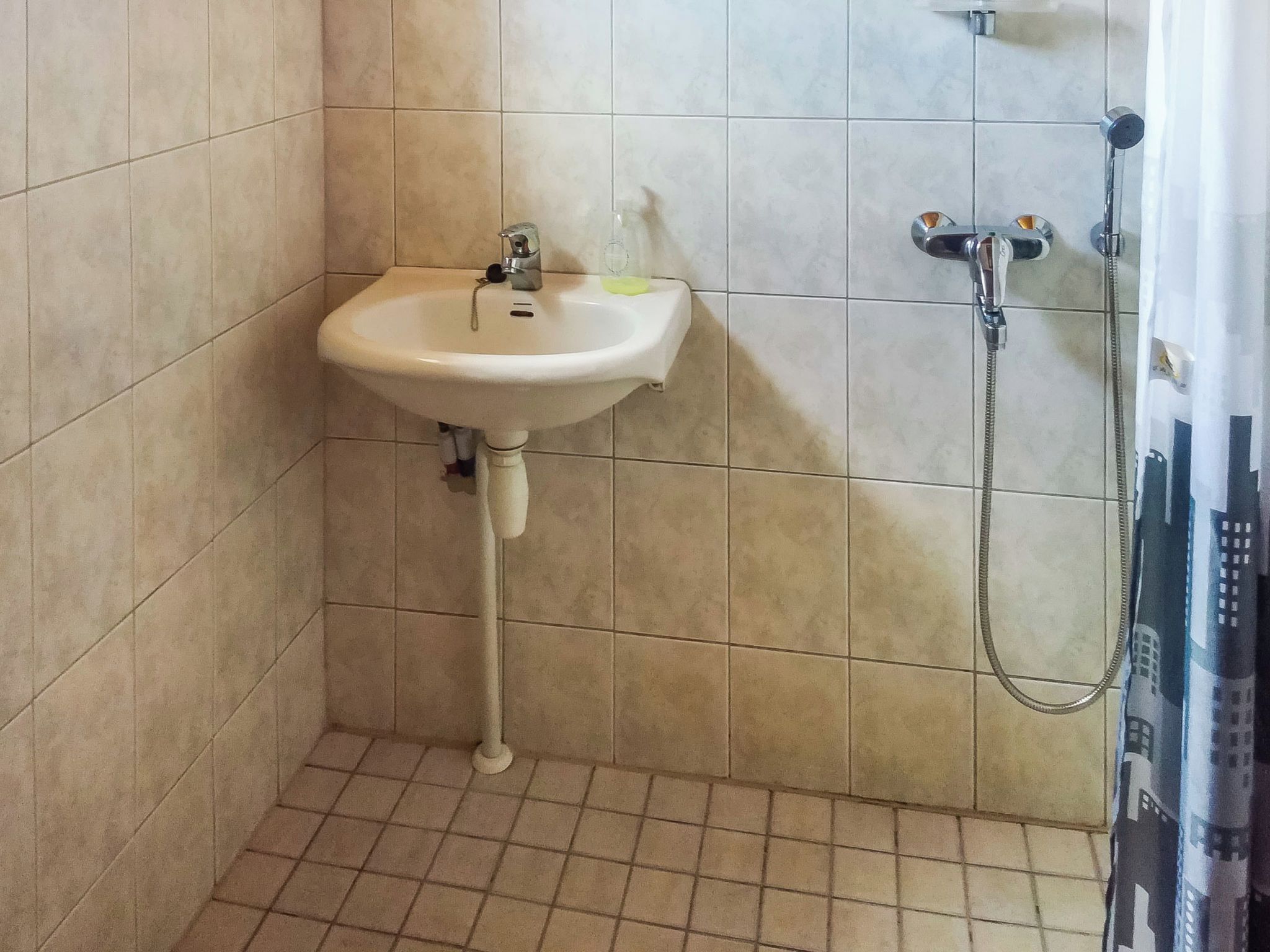A bathroom with a pedestal sink, a handheld showerhead, and tiled walls.