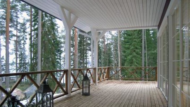 A wooden deck with a railing, large windows, and a view of tall trees. - Ylä-hannala by Interhome (Muurame)