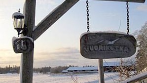 A wooden signpost with a sign that reads "Jouarikopka" in a rural setting with snow-covered ground and a clear sky.
