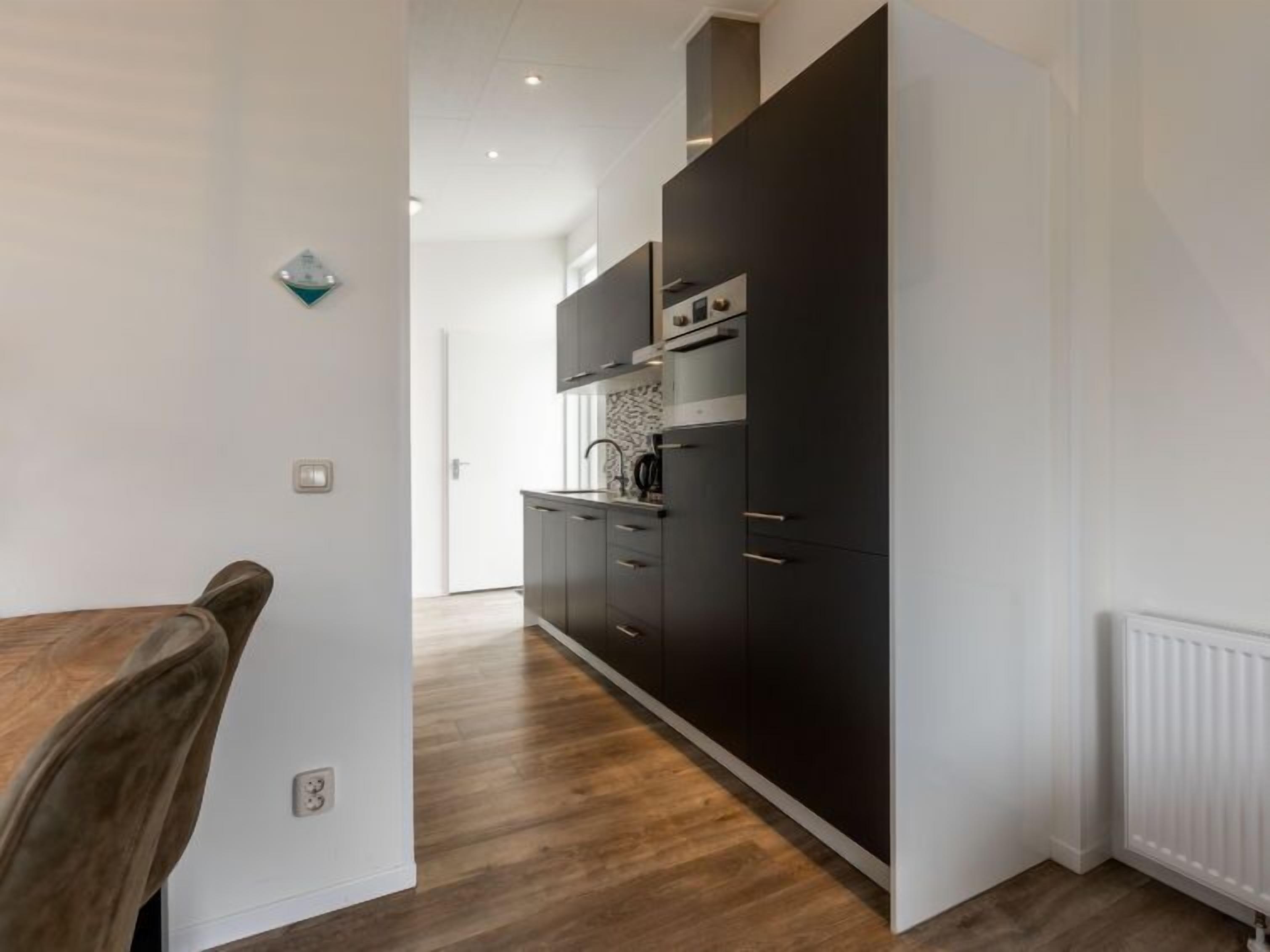 Une cuisine moderne avec des meubles de couleur sombre, une hotte en acier inoxydable et une table à manger en bois.