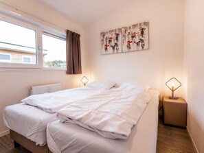 Ein Schlafzimmer mit einem Bett, zwei Nachttischen, einem Fenster mit Vorhängen und einer Wand mit Kunstwerken.