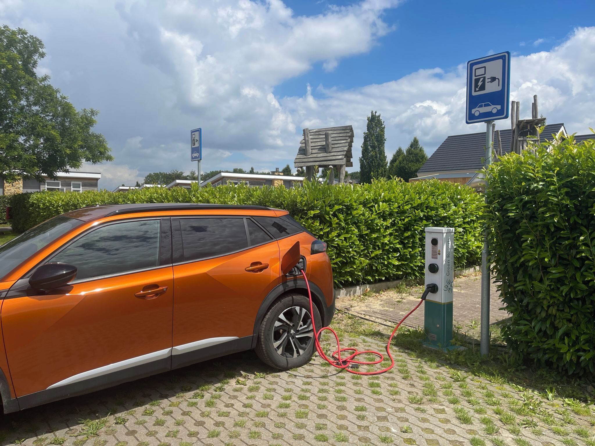 An orange electric vehicle charging at a station with a sign indicating a parking area.