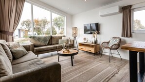 A modern living room with a sofa, a coffee table, a TV, and a dining area. - Green Resort Mooi Bemelen by Interhome (Bemelen)