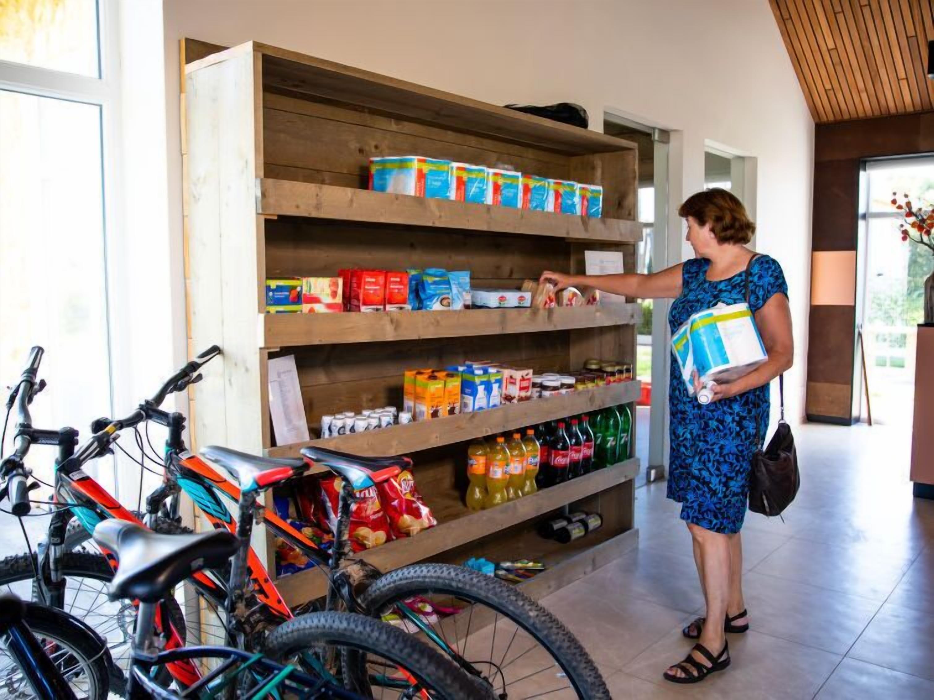 A woman in a blue dress reaching for items on a shelf in a room with bicycles and a wooden floor.
