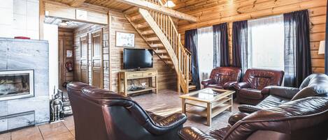 Un salon chaleureux avec des canapés en cuir, un escalier en bois, une cheminée et un téléviseur.