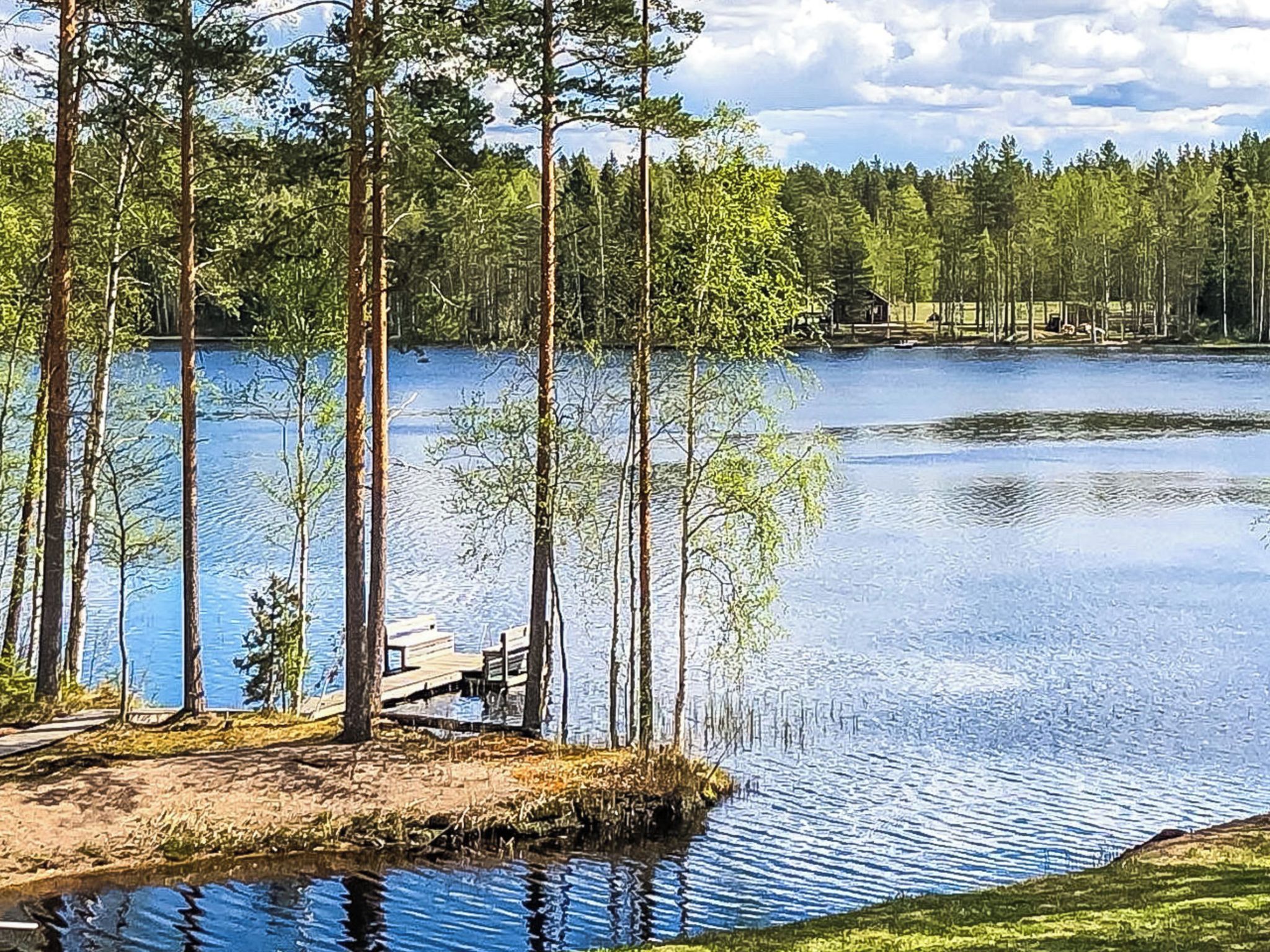 A lakeside view with a dock, trees, and a cabin in the distance.
