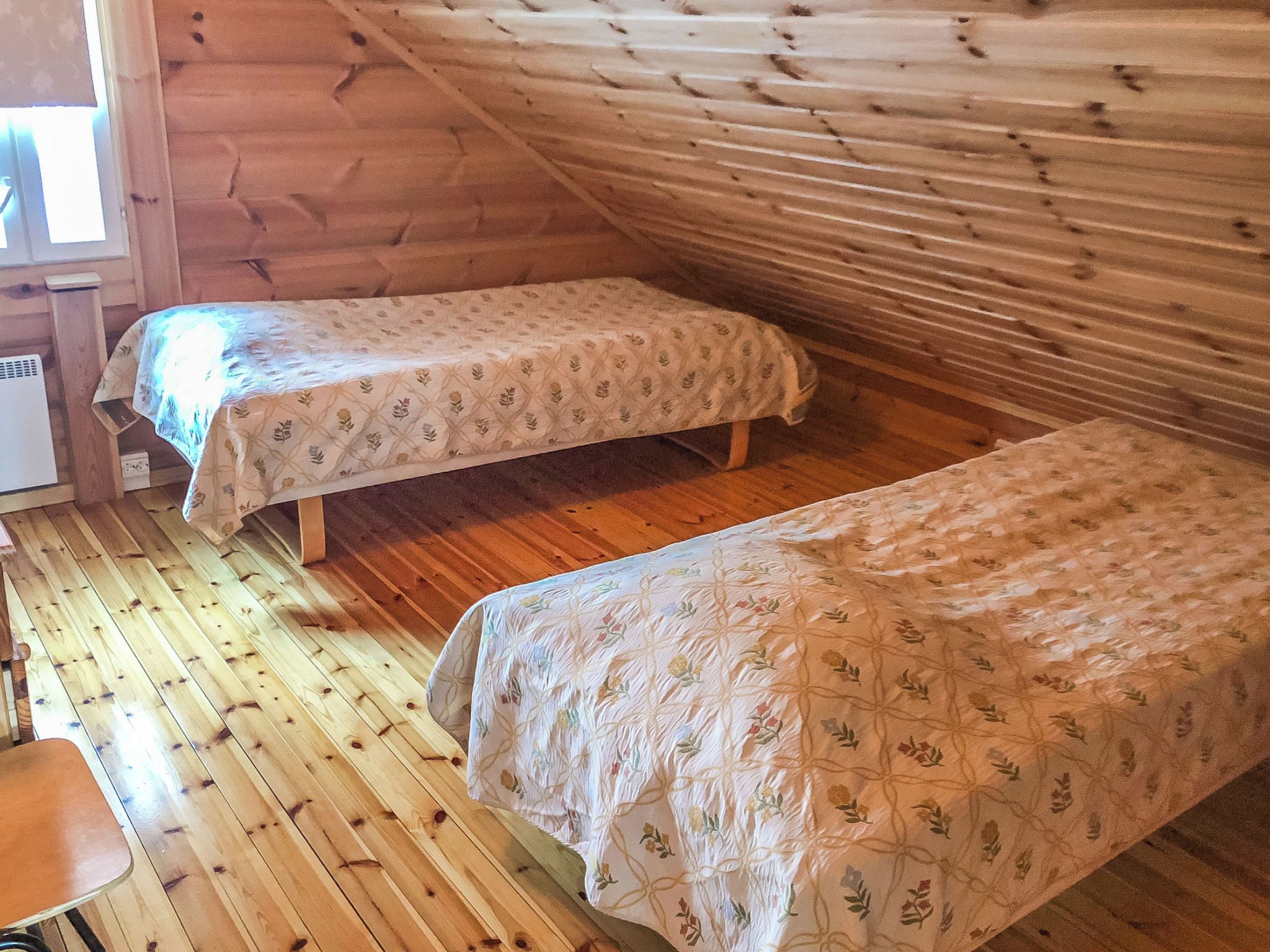 A cabin with two beds, wooden floors, and a window.