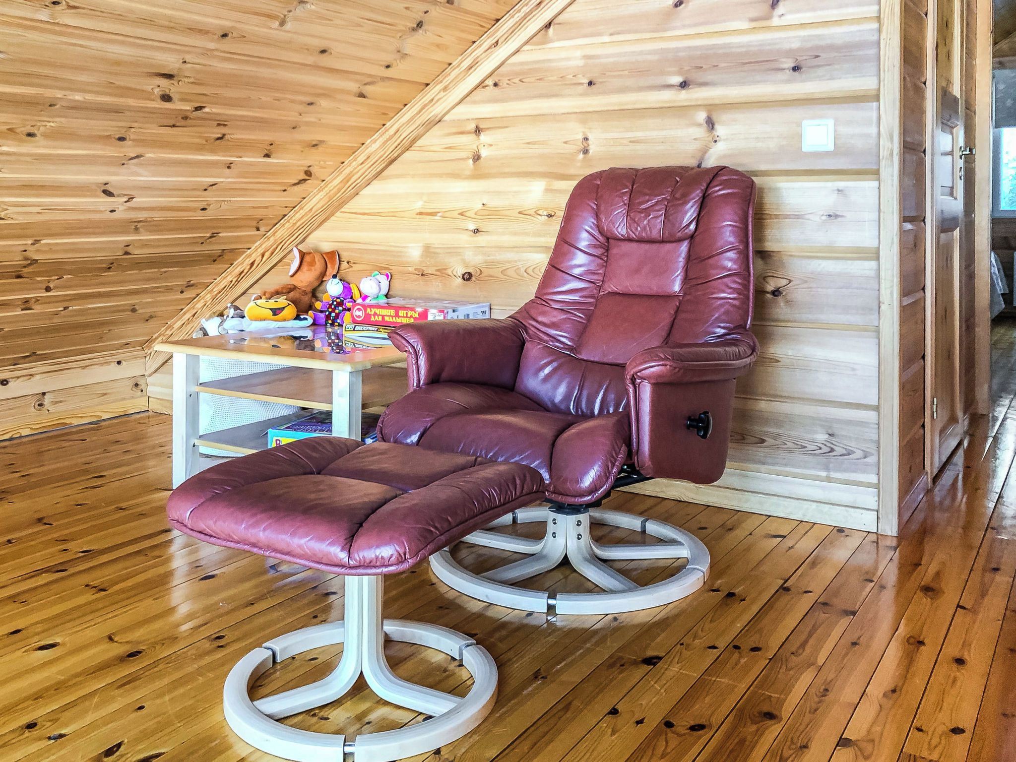 A room with a wooden sloped ceiling, a leather recliner chair, and a small table with toys and books.