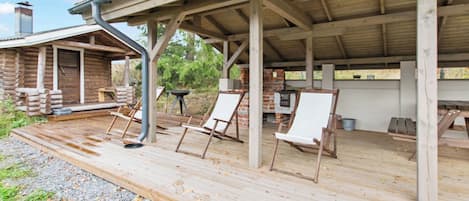 Een overdekt buitengebied met houten terras, twee lounge fauteuils en een schouw van baksteen.