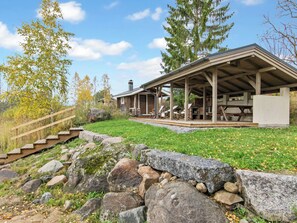 Un chalet rustique doté d’un patio couvert, d’un mur de soutènement en pierre et d’un escalier en bois menant à l’entrée.