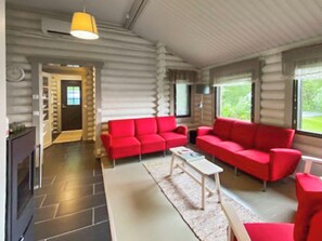 A log cabin interior with a red sofa set, a white coffee table, and a yellow hanging light fixture. - Pihlajakumpu by Interhome (Petäjävesi)