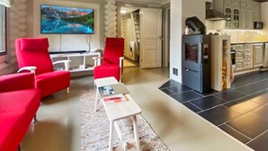 Ein Wohnzimmer mit roten Sesseln, einem weißen Couchtisch und einem Fernseher, der eine Berglandschaft zeigt.