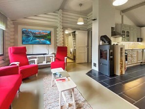 Un salon moderne avec des fauteuils rouges, un téléviseur à écran plat et un coin cuisine équipé de placards et d’un réfrigérateur.