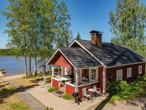 Une cabane rouge avec un porche, des sièges d’extérieur et un barbecue.
