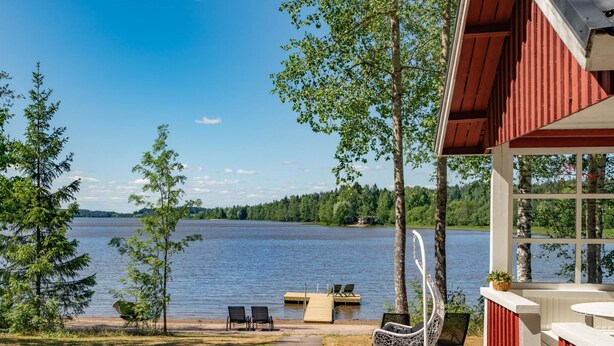 Una cabaña junto al lago con asientos exteriores, un muelle y vistas al lago y al bosque.