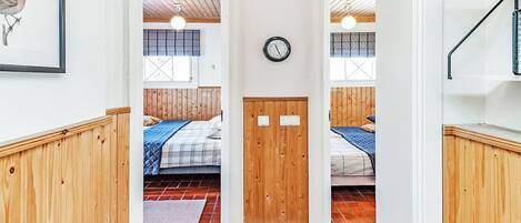 Un couloir étroit mène à deux chambres dotées de planchers en bois, une horloge est accrochée au mur et, sur la gauche, on peut voir un tableau encadré.
