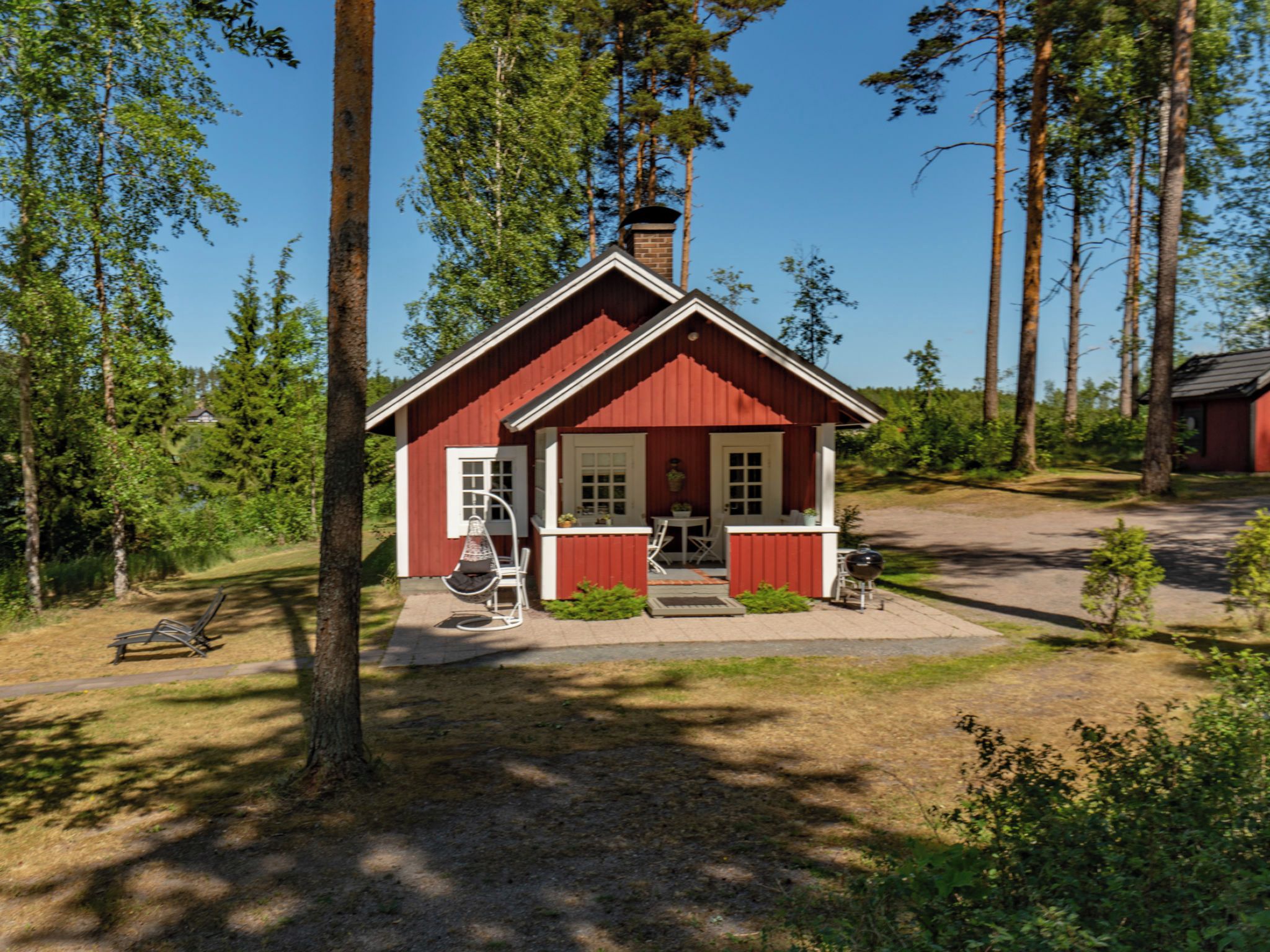 A red cabin with a chimney, surrounded by trees, and a bench nearby.