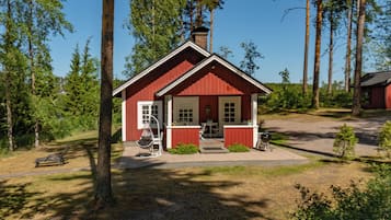 A red cabin with a chimney, surrounded by trees, and a bench nearby.