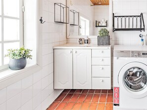 Ein modernes Badezimmer mit weiß gefliesten Wänden, einem Waschbecken mit Spiegel, einer hängenden Pflanze und einer Waschmaschine.