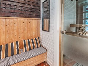A wooden bench with striped cushions against a white brick wall, a wooden door with a glass panel, and a metal hookboard above the bench. - Sepelkyyhky by Interhome (Somero)