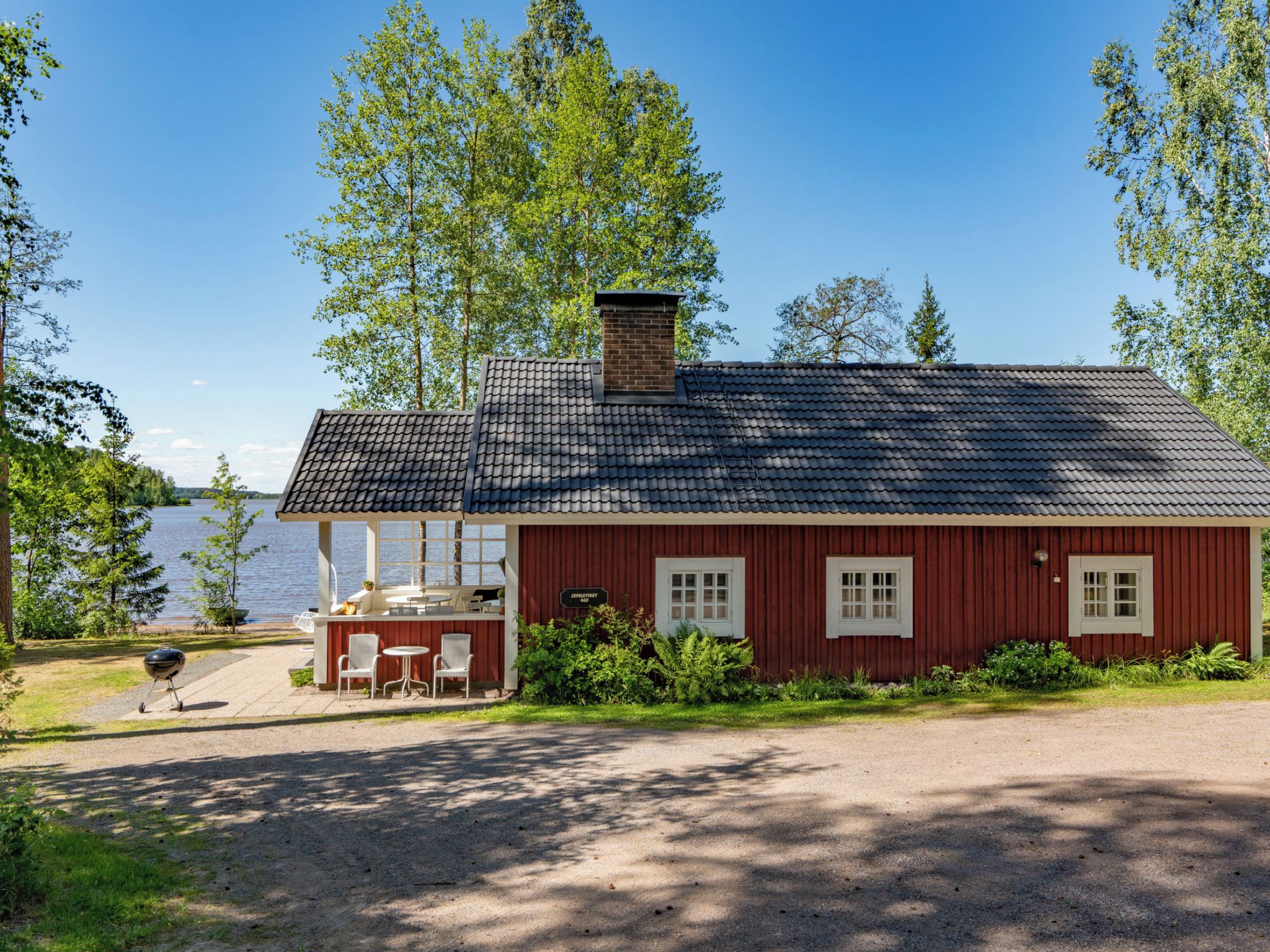 A red wooden cabin with a tiled roof, a small porch with chairs, and a grill outside.