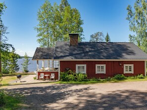 A red wooden cabin with a tiled roof, a small porch with chairs, and a grill outside. - Sepelkyyhky by Interhome (Somero)