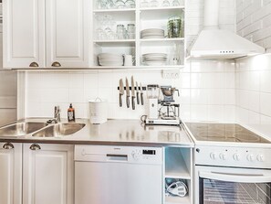 Eine moderne Küche mit weißen Schränken, einem Geschirrspüler, einem Backofen und einer Kaffeemaschine.