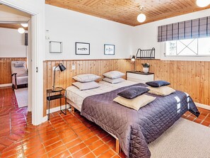 A bedroom with a wooden headboard, a bed with multiple pillows, a nightstand, a floor lamp, and a window with a view.