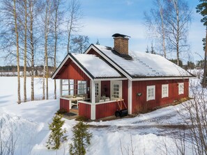 Eine rote Holzhütte mit Schornstein, Veranda und Blick auf eine verschneite Landschaft.