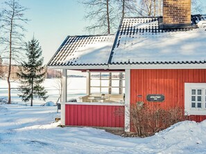 Un bâtiment en bois rouge, avec un toit recouvert de tuiles et une grande fenêtre, entouré de neige.