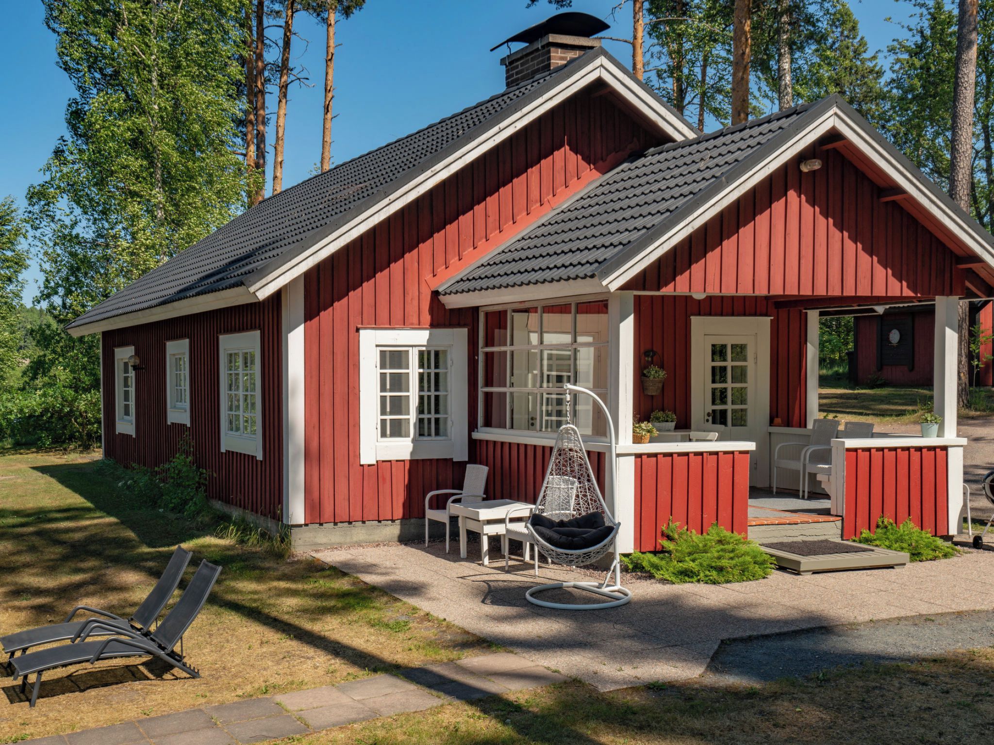 A red wooden cabin with a porch, a hanging chair, and a table with chairs.