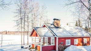 Una casa de madera roja con techo inclinado, chimenea y un porche con mobiliario exterior.