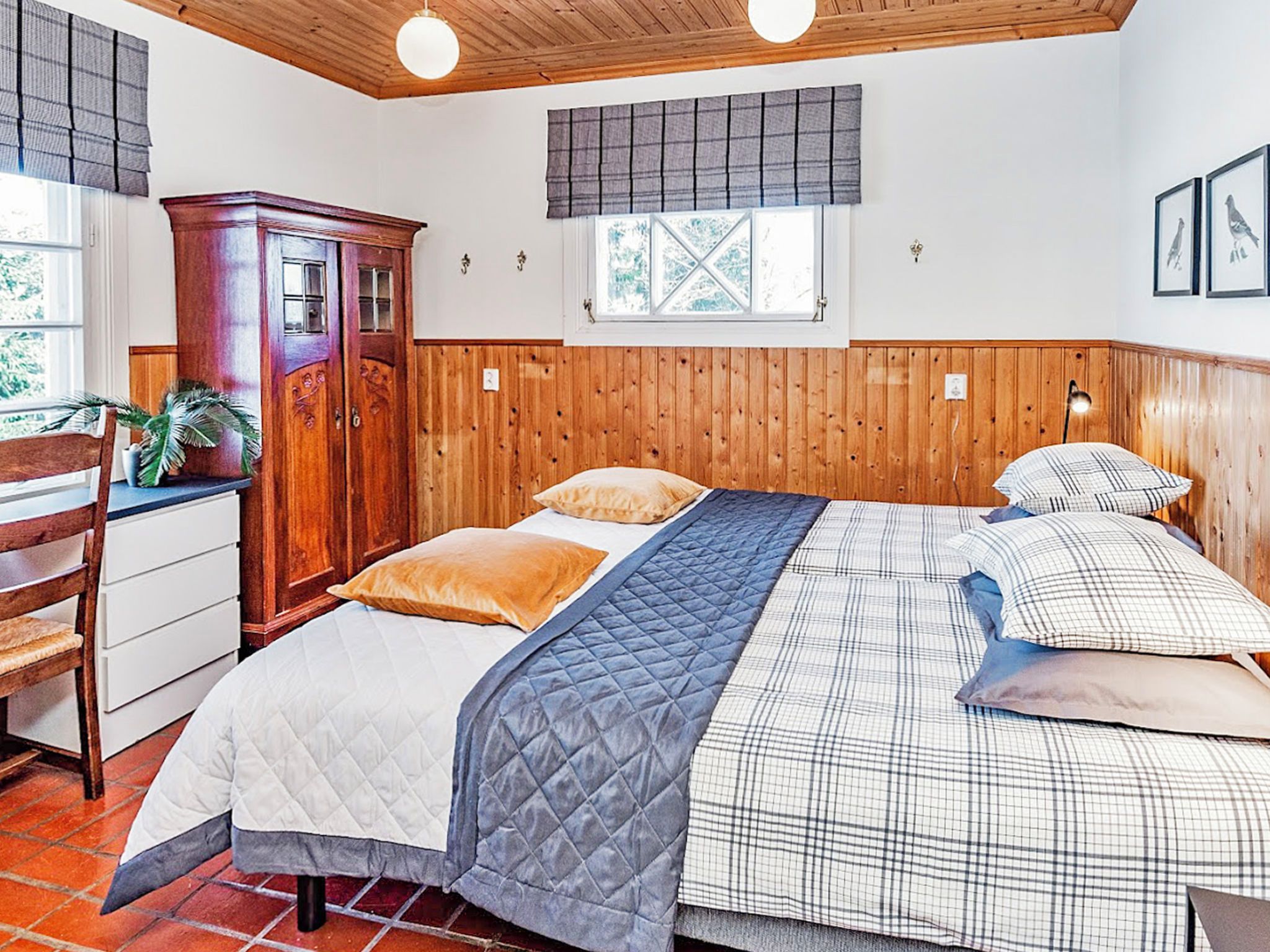 Un dormitorio con cabecera de madera, cama con colcha acolchada, dos almohadas, una mesita de noche y un armario de madera.