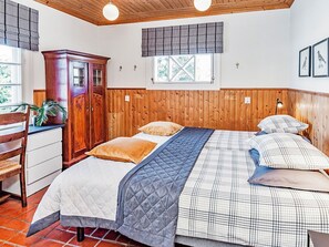 Un dormitorio con cabecera de madera, cama con colcha acolchada, dos almohadas, una mesita de noche y un armario de madera.