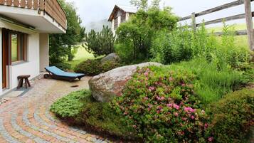 Ein Garten mit einem Pflasterweg, einem blauen Liegestuhl und einem großen Felsen.