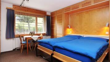 Une chambre à coucher avec un lit double, une tête de lit en bois, un bureau avec une chaise et une fenêtre avec des rideaux.