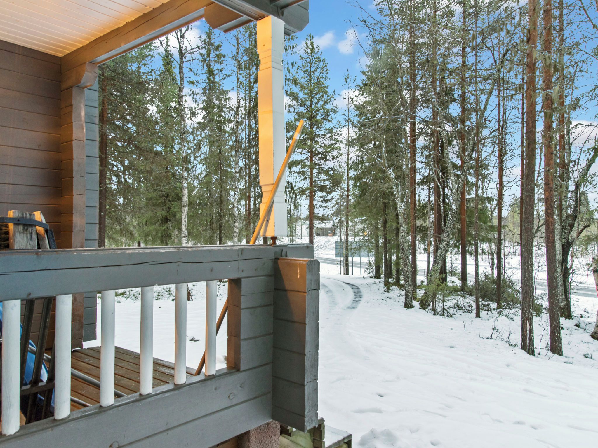 A wooden deck with a railing overlooking a snowy landscape with trees.