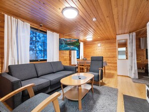 Ein gemütliches Blockhaus-Interieur mit einer Couch, Sesseln, einem Couchtisch und einem an der Wand befestigten Fernseher.