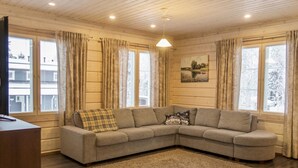 Un salon chaleureux avec un canapé d’angle, un plancher en bois et de grandes fenêtres dotées de rideaux.