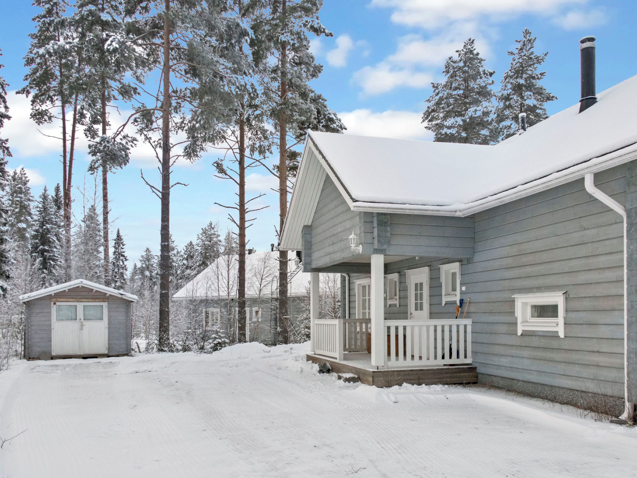 Ett tvåvåningshus med en veranda, omgivet av snötäckta träd.