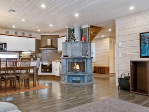 A modern interior with a stone fireplace, wooden flooring, and a kitchen area. - Villa sofia by Interhome (Sotkamo)