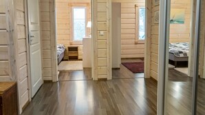 L’intérieur d’un chalet en bois comprend un couloir qui mène à deux chambres, chacune étant dotée d’une fenêtre et d’un lit.
