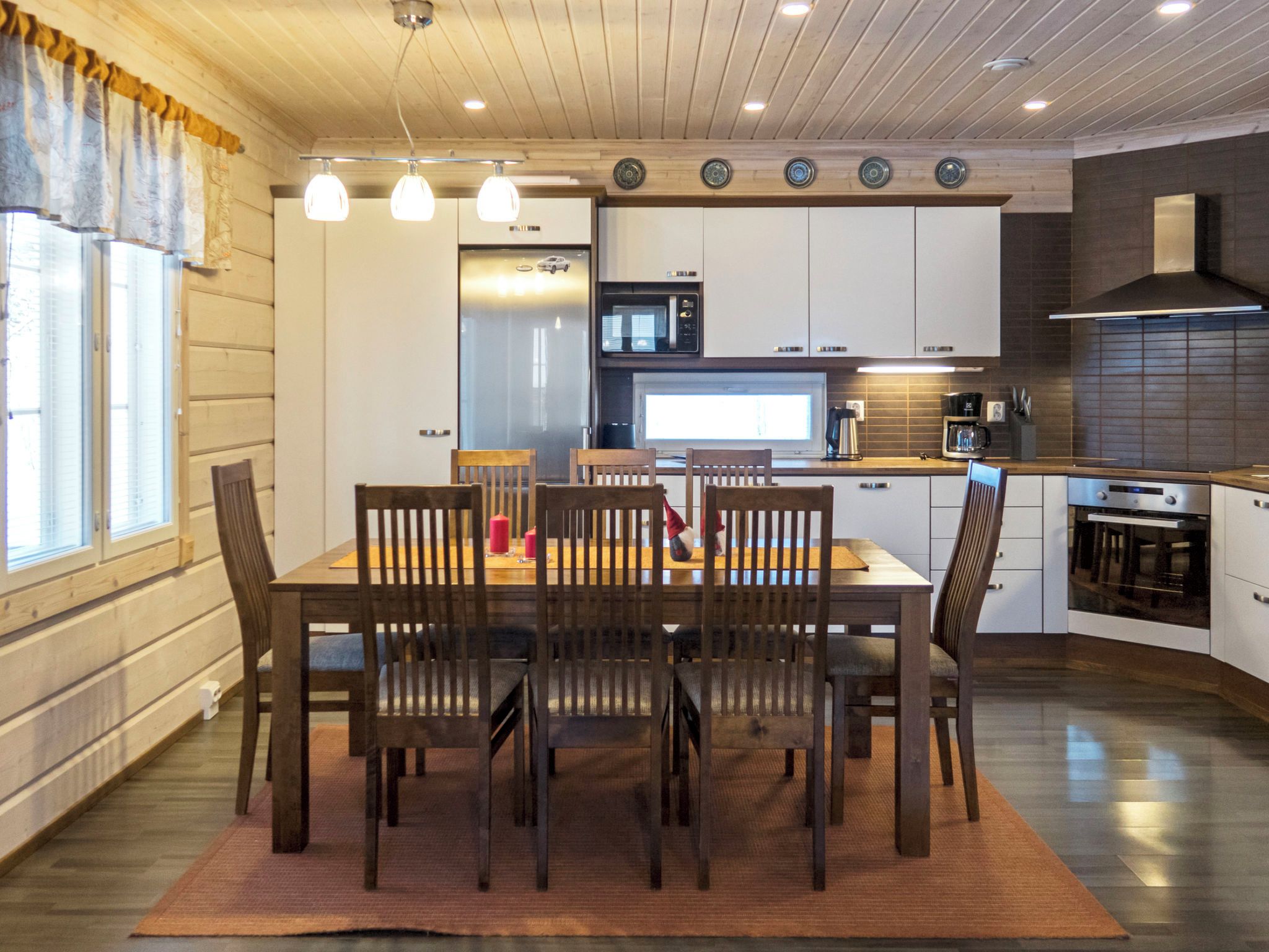 A modern kitchen with a dining area, featuring a wooden table and chairs, a built-in oven, and a microwave.
