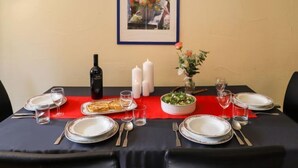 A dining table set with plates, cutlery, glasses, and a bottle of wine, with a framed floral artwork above.